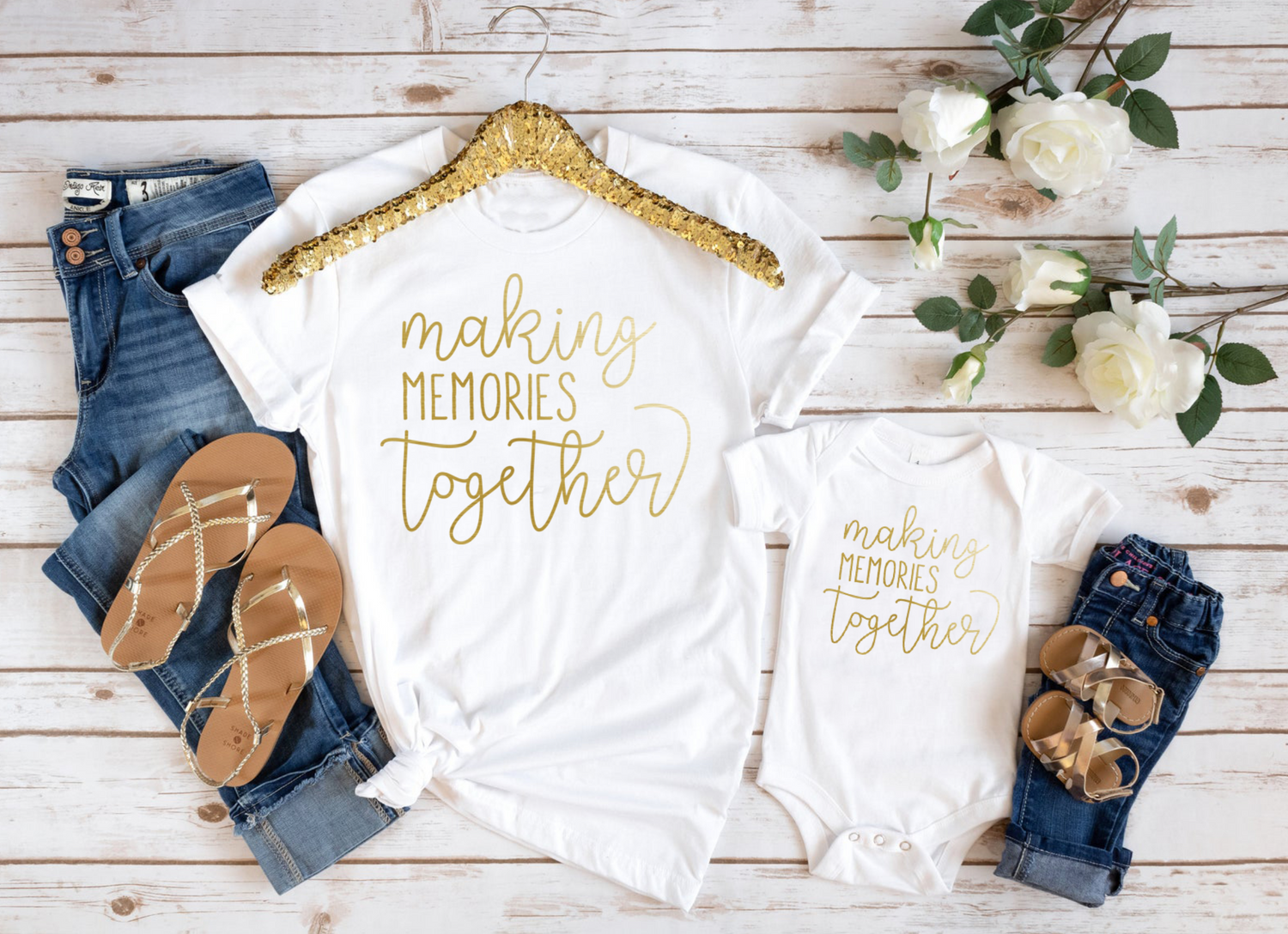 Matching 'Making Memories Together' t-shirts in white with gold foil print, displayed with jeans and sandals on a wooden background.